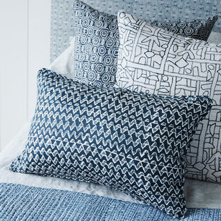 Self welt pillow linen slate with triangular block print pattern with two other pillows on a bed.