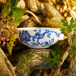 Caskata Arcadia Vegetable bowl with blue floral patterns on a natural background with leaves and twigs.
