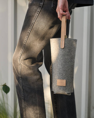 Graf Lantz wine carrier in grey merino wool felt with light natural leather handle and label carried by a person in black jeans.