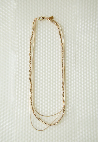 Zeta necklace by Abacus Row.
 Triple-stranded design featuring one complete strand of our Signature Leo beadwork layered with two continuous fluid gold strands.

Length – 16.5"

Materials – 14k gold-filled beads and findings, silk cord