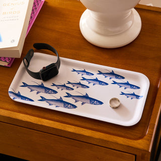 White tray with blue fish pattern on a wooden surface with a watch and ring.