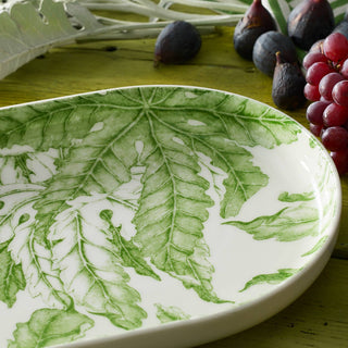 White plate with green leaf pattern on a wooden surface with figs and grapes.