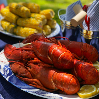 Platter of lobsters with corn on the cob and lemons on a table outdoors.