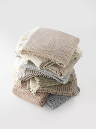 Stack of folded textured blankets in beige, brown, and gray on a white background