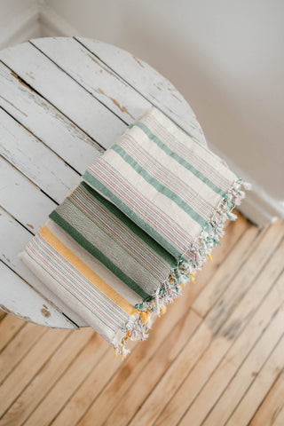 Stack of three Home & Loft turkish towels on a small rustic table.