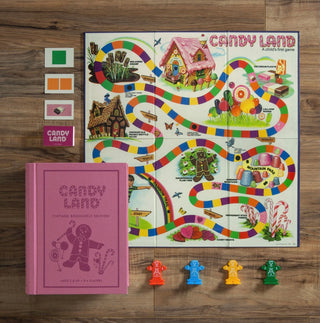 Candy Land Vintage Bookshelf Edition Game  by WS Game Company.
Fabric wrapped book with integrated storage with:
Full-sized vintage gameboard with graphics adopted from the 1978 edition- Candy Land
Deck of vintage cards
4 “Frosted” plastic Gingerbread Men playing pieces
Instructions