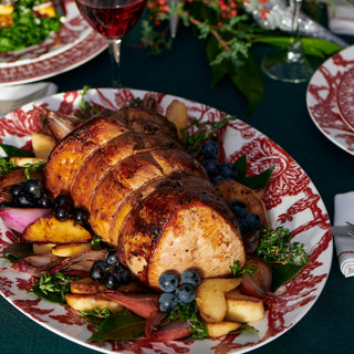 A sliced roasted meatloaf or pork loin served on a red-and-white patterned platter with fruit, blueberries, and herbs on a dark table setting.