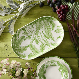 Green and white leaf-patterned ceramic platter on a wooden surface with decorative elements.