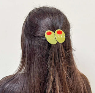 A pair of novelty hair clips shaped like cartoonish green eyes with red pupils, shown clipped to a half-updo of dark brown hair against a plain off-white background.