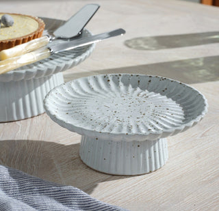 Speckled cake stand in white salt glaze by Blue Pheasant. Dimensions 7.5”Dx 2.75”H