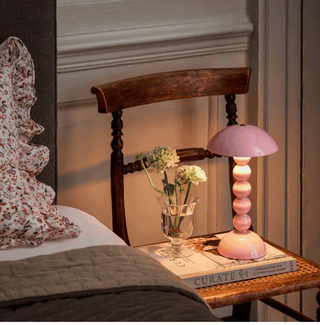 Addison Ross pale pink bobbin cordless table lamp on a bedside chair with a book and a vase of fresh wildflowers.