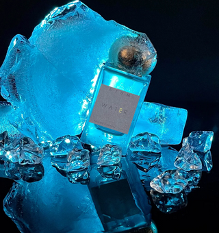 Bottle of Atum Water fragrance with gold top surrounded by ice cubes on a dark background.
