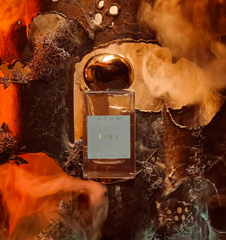 Atum Fire fragrance bottle with gold top set in front of a smokey, firey backdrop.