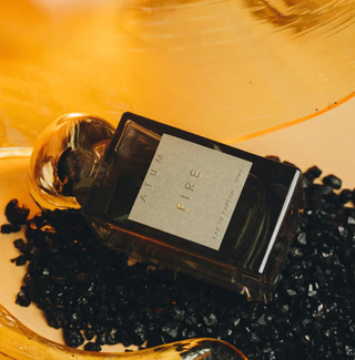 Atum grey glass bottle with amorphous gold top and elegant grey box with Atum Fire written on the front in grey and gold set on top of an amber and coal backdrop.