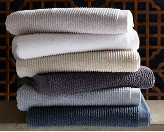 Matouk Aman stack of folded towels in various colors on a wooden surface with a decorative background.