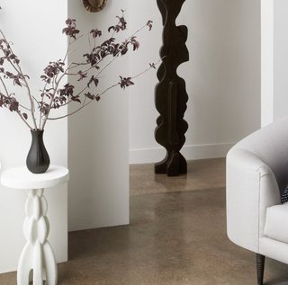 Modern interior with a vase of branches on a white side table, a dark wooden sculpture, and a white sofa.
