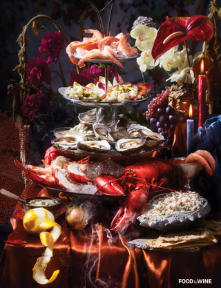 Piecework Puzzles three-tiered seafood platter with oysters, shrimp, and lobster on a dark background with candles and flowers. Food & Wood