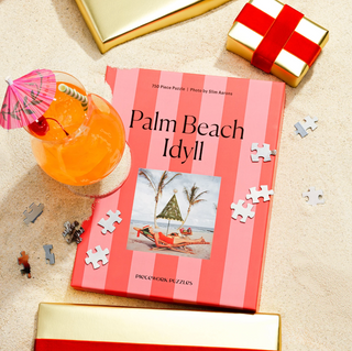 Piecework Puzzles Palm Beach Idyll puzzle book with a cocktail and scattered pieces on sand