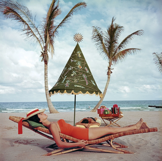 Piecework Puzzles Palm Beach Idyll Woman lounging on a beach with palm trees and a decorative umbrella