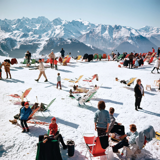 Piecework Puzzles Verbier Vacation puzzle picturing people enjoying a sunny day on a snowy mountain with colorful chairs and mountains in the background.