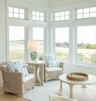 Sunroom with Made Goods Jayceon whitewashed Lampakanay armchair with white cushion featuring large windows with a scenic view.