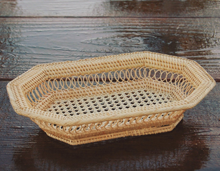 A natural woven rattan basket with an octagonal shape and open lattice design, placed on a dark wooden surface.