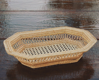 A natural woven rattan tray with an octagonal shape and open lattice design, displayed on a dark wooden surface.