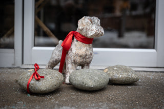 Stone dog figurine with a red ribbon on a snowy ground