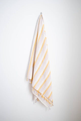 Home & Loft turkish towelwith yellow stripes hanging on a hook.