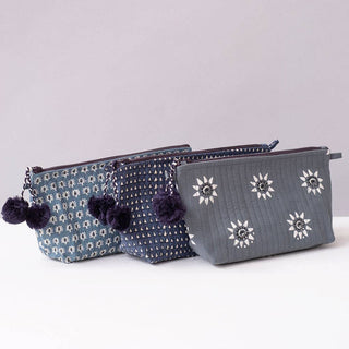 Three gray pouches with floral patterns and pom-poms on a light background