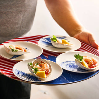 Person holding a tray with four small plates of seafood and lemon wedges.