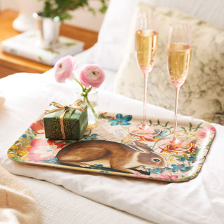 Decorative tray with a rabbit design, gift, and champagne flutes on a floral-patterned surface.
