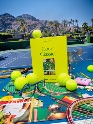 Book titled 'Court Classics' on a tennis court with tennis balls and a racket.