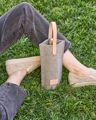 Graf Lantz wine carrier in grey merino wool felt with light natural leather handle and label next to a person sitting on the grass.