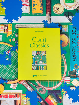Piecework Puzzles Court Classics puzzle. Yellow book titled 'Court Classics' on a colorful puzzle background with various items.
