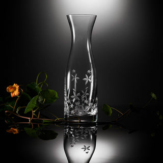 Clear glass carafe with floral etching on a reflective surface with dark background