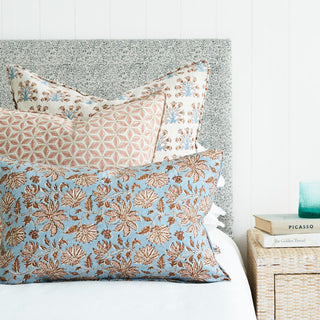 Self welted blue linen pillow with tobacco and off white floral pattern on a bed with two other throw pillows.